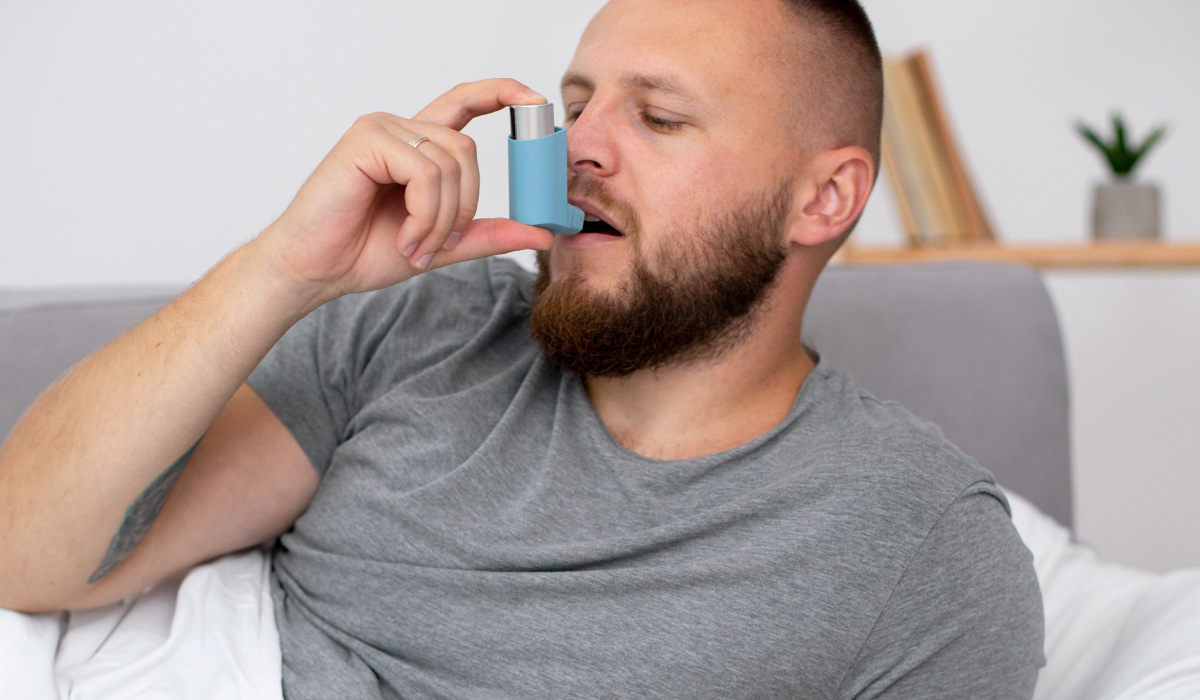 Hombre usando un inhalador para el asma, en la comodidad de su hogar, buscando alivio para sus síntomas respiratorios